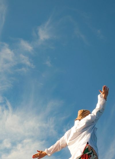 A joyful woman with arms spread wide looks to the sky, capturing the essence of freedom and summer.